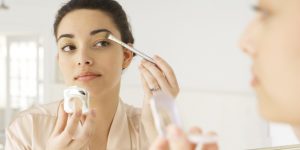 Young woman applying make-up in mirror, using brush, close-up